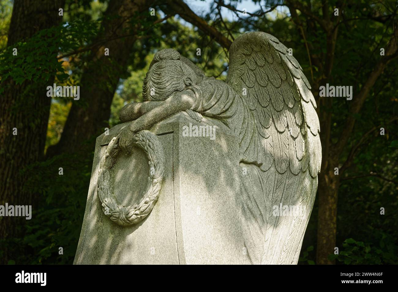 2023 - Lowell Cemetery - Lowell, MA. Eine herzzerreißende Gedenkstätte aus weißem Marmor eines Engels, der in den Stein weint, der einen Kranz hält und ihre Flügel freigelegt hat. Stockfoto