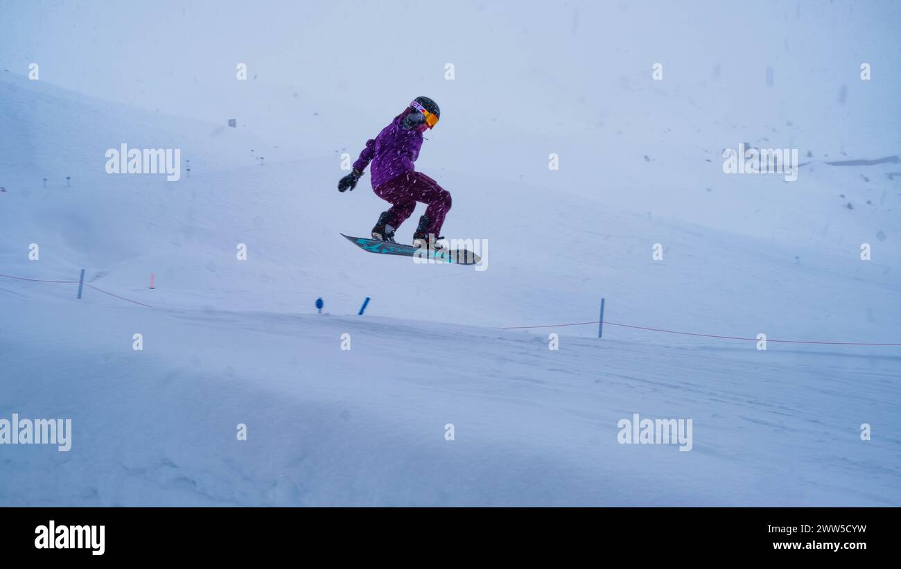 Lila Snowboarder springt im Park in die Luft, während der Schnee fällt Stockfoto