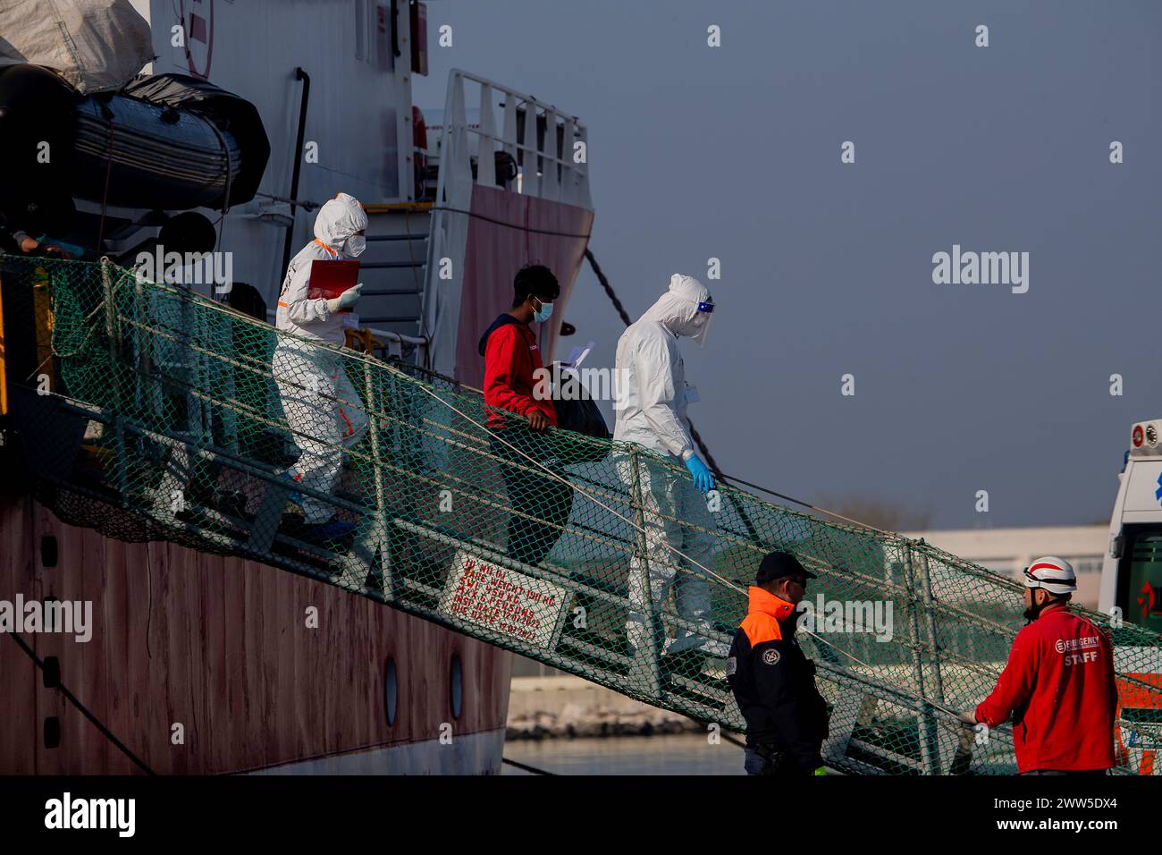 Ravenna, Italien. März 2024. Gesundheitskontrollärzte begleiten einen Migranten, der aus dem Schiff aussteigt, das im Hafen von Ravenna angekommen ist das Rettungsschiff Life Support landete um 8:00 Uhr morgens im Hafen von Ravenna mit 71 Migranten an Bord, die während ihrer Schifffahrt auf See gerettet wurden. (Foto: Marco Cordone/SOPA Images/SIPA USA) Credit: SIPA USA/Alamy Live News Stockfoto