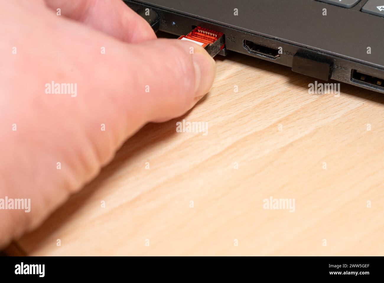 Stecken Sie einen hellgrauen Netzwerkstecker, der an ein CAT 7-Netzwerkkabel angeschlossen ist, von Hand in einen schwarzen Laptop. Stecker ist bereits im Steckplatz. Stockfoto