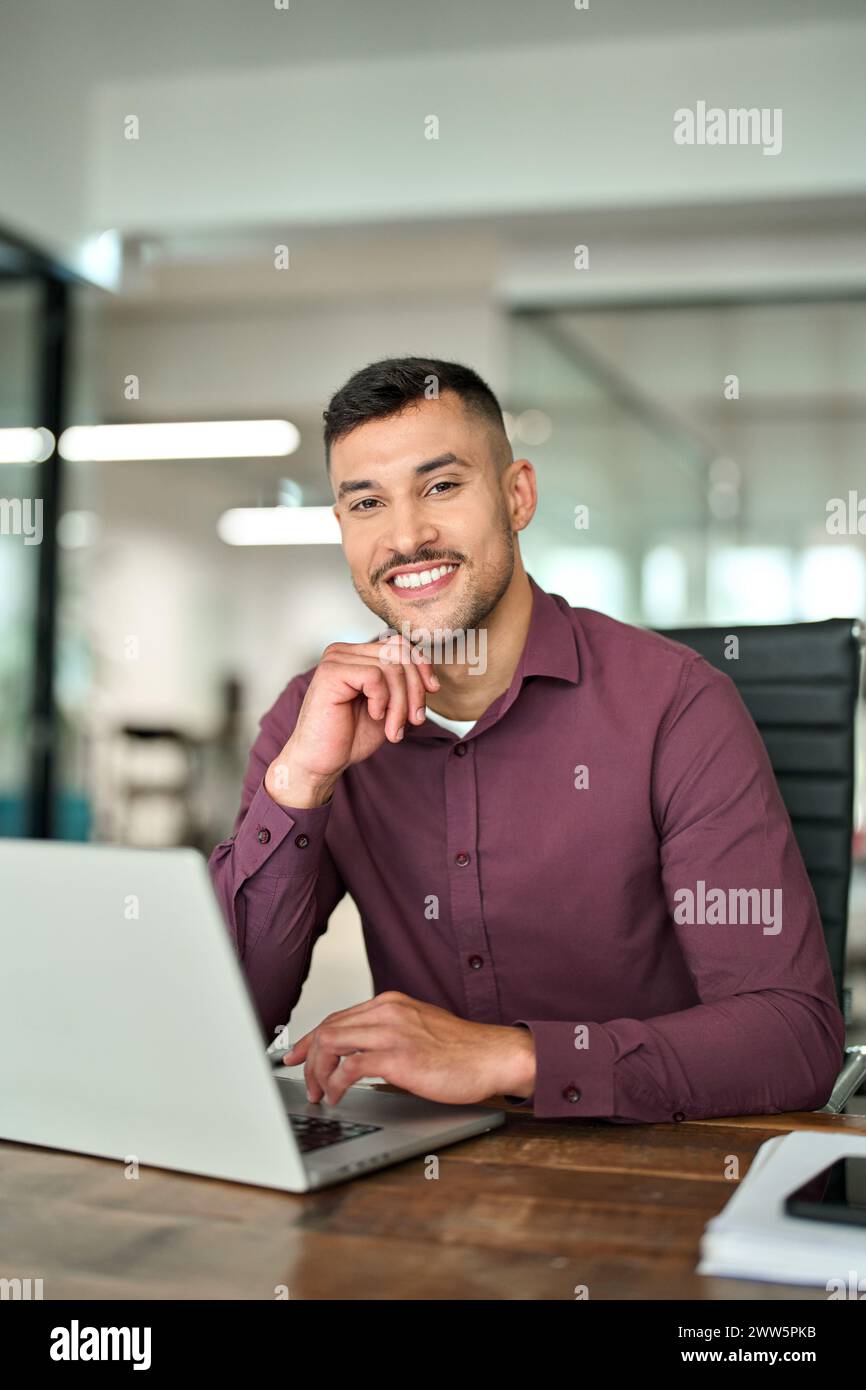 Glücklicher lateinamerikanischer Geschäftsmann, der bei der Arbeit auf die Kamera schaut, vertikales Porträt. Stockfoto
