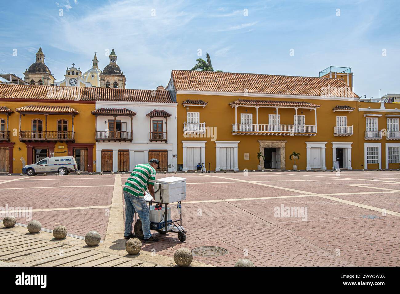 Cartagena, Kolumbien - 25. Juli 2023: Straßenverkäufer verkauft kalte Getränke auf der Plaza de la Aduana. Santuario de San Pedro Claver Top mit Türmen und Uhr pe Stockfoto