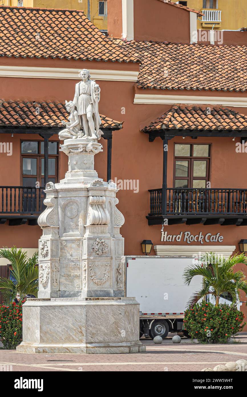 Cartagena, Kolumbien - 25. Juli 2023: Weißes hohes Cristobal Colon Monument auf der Plaza de la Aduana. Hard Rock Cafe direkt dahinter in braunem Kolonialarchitekten Stockfoto