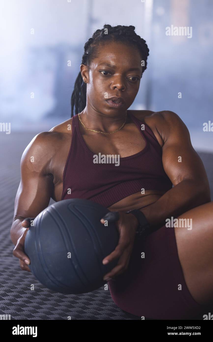 Eine afroamerikanische Frau mittleren Alters hält einen Medizinball im Fitnessstudio Stockfoto