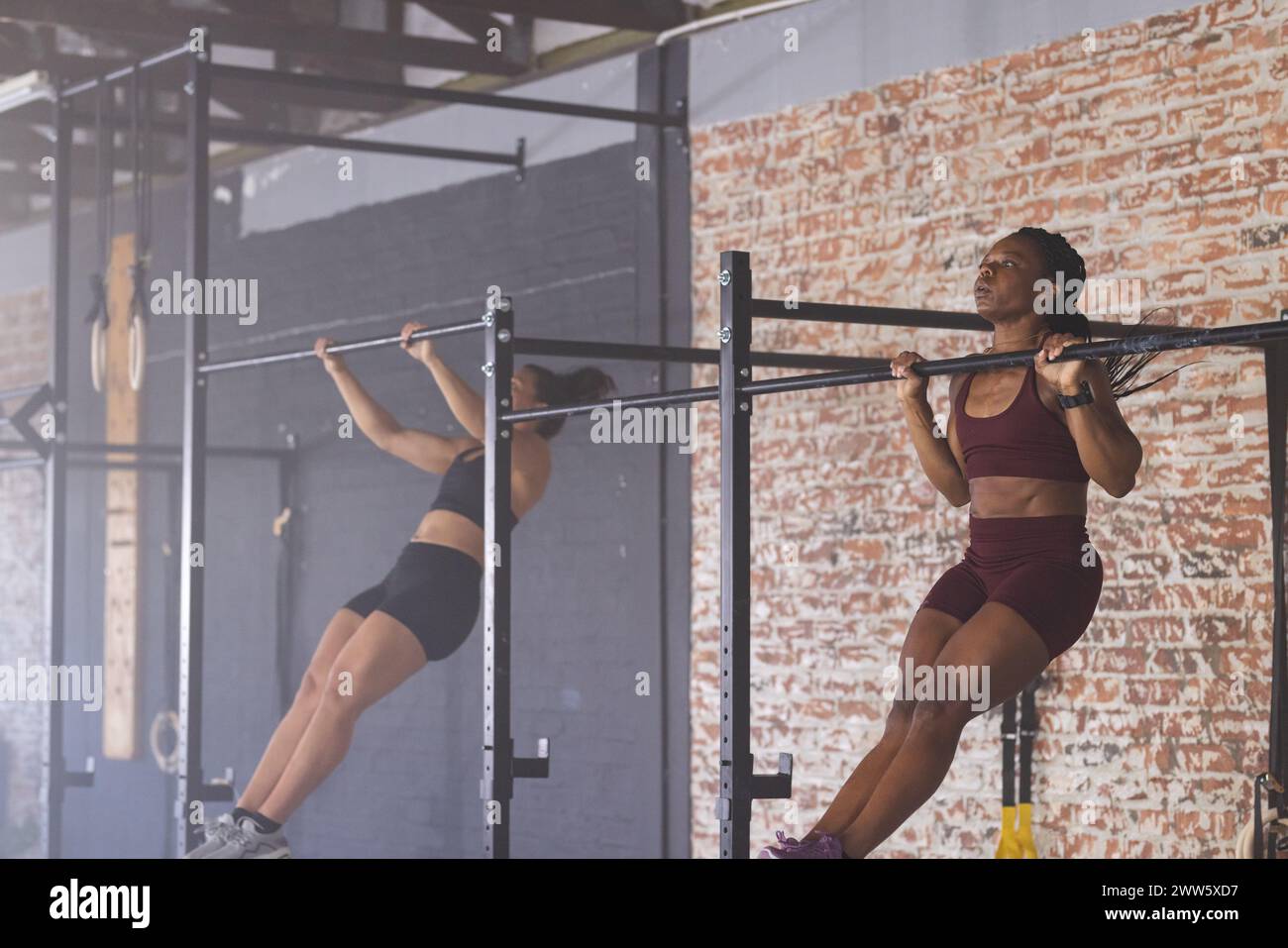 Zwei Frauen mit variabler Passform nehmen im Fitnessstudio an einem Pull-up-Workout Teil Stockfoto