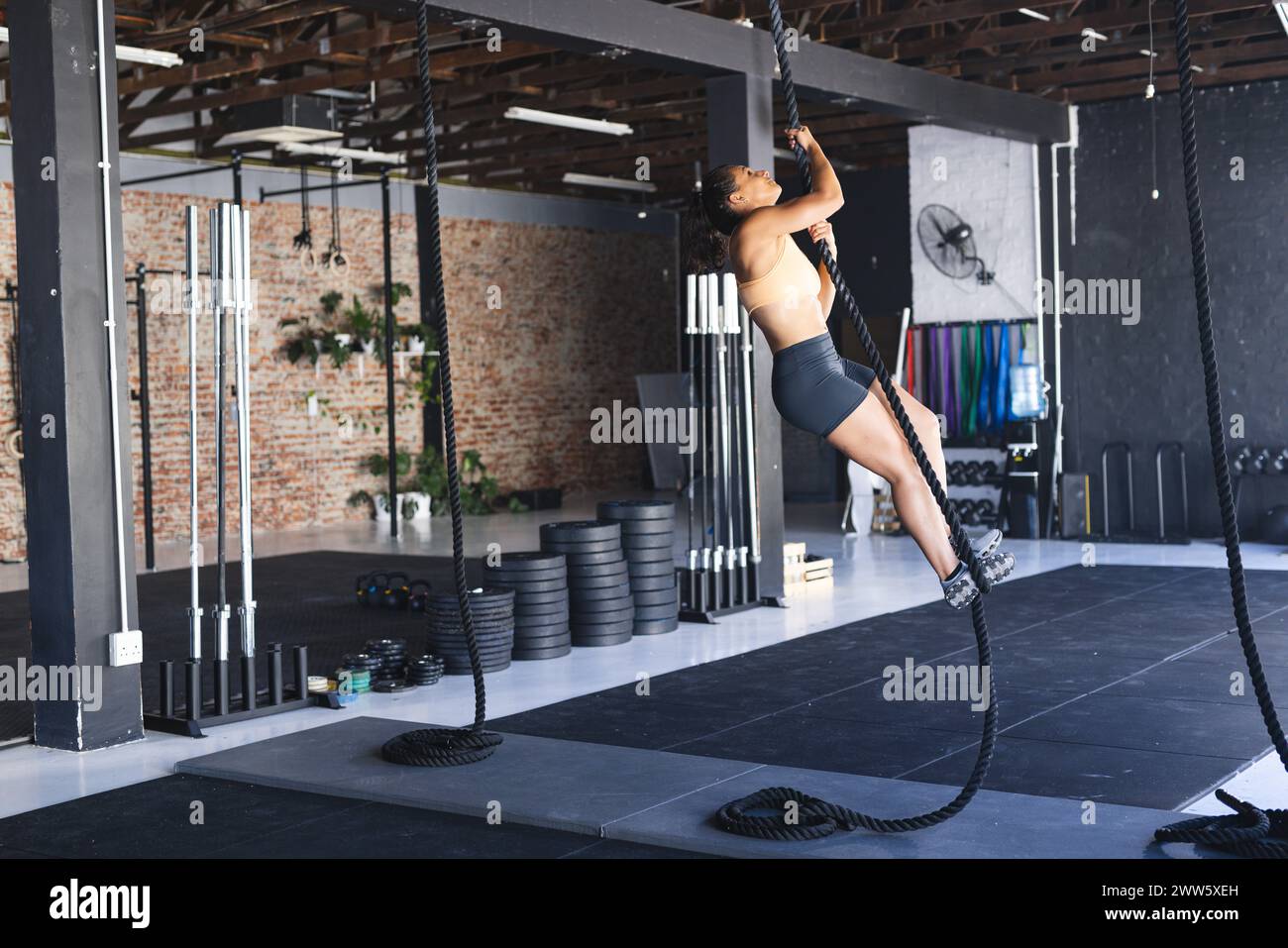 Eine fitte weiße Frau klettert im Fitnessstudio mit Entschlossenheit an ein Seil, mit Kopierraum Stockfoto