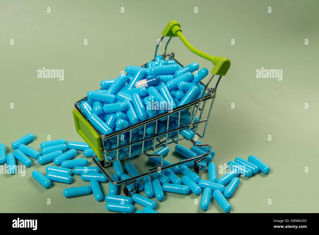 Blaue Pillen in einem Einkaufswagen auf grünem Hintergrund. Das Konzept des Arzneimittelkaufs. Blaue Pillen in einem Einkaufswagen auf grünem Hintergrund. Kaufkonzept Stockfoto