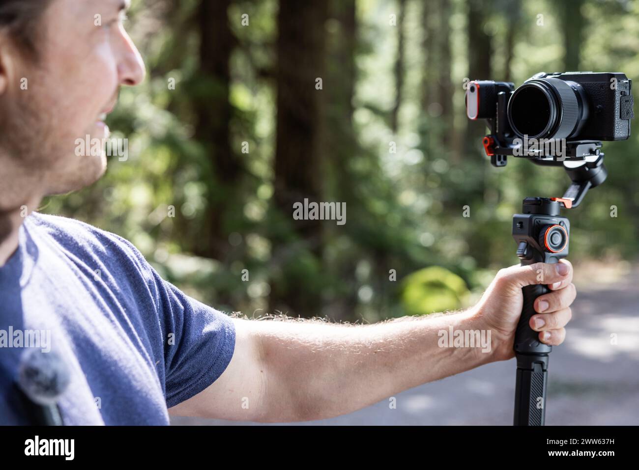 Content Creator verwendet ein Kamera-Gimbal, um in der Natur mit einem verschwommenen Wald im Hintergrund zu filmen Stockfoto