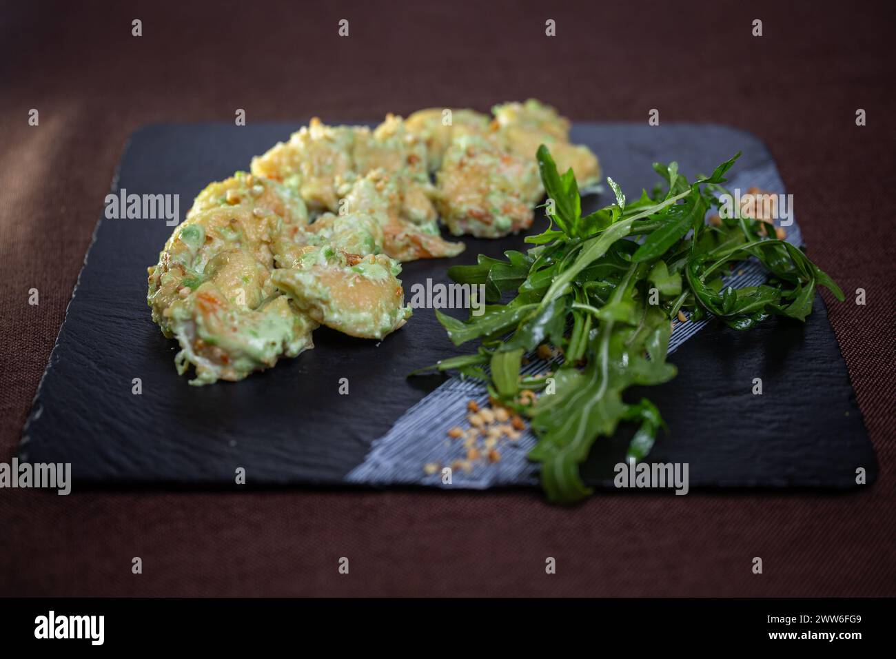 Eine Nahaufnahme frittierter Avocadogarnelen mit Rucola auf einem schwarzen Steinteller, perfekt für Meeresfrüchte-Liebhaber. Stockfoto