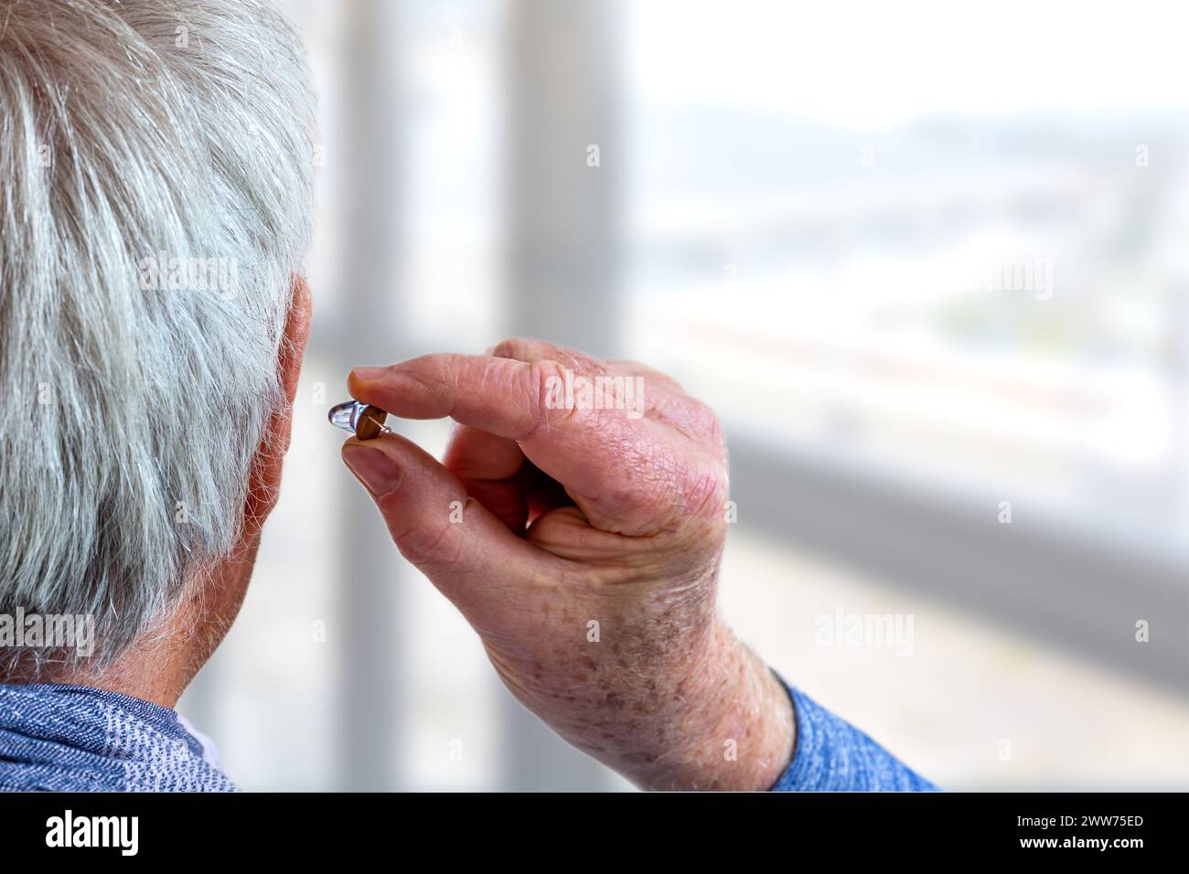 Amerikanischer Schuss, ein Hörgerät an einen weißhaarigen Senioren anzubringen, Rückansicht. Stockfoto