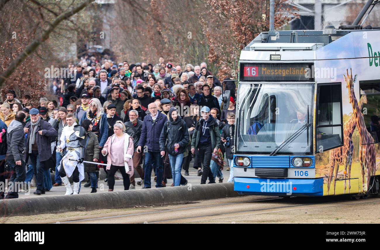 22. März 2024, Sachsen, Leipzig: Eine LVB-Straßenbahn fährt am Morgen zu Fuß an zahlreichen Besuchern vorbei zur Leipziger Messe. Die Leipziger Verkehrsgesellschaft streikt seit den frühen Morgenstunden durch die gewerkschaft Verdi. Nach Angaben des Unternehmens werden die Straßenbahnverbindungen zum Messegelände jedoch mit nicht streikenden Fahrern aufrechterhalten. Über 2000 Aussteller aus 40 Ländern werden ihre neuen Produkte auf dem Frühjahrstreffen der Buchbranche präsentieren. Unter dem Motto "alles außer flach" werden die Niederlande und Flandern als Gastländer vertreten sein Stockfoto