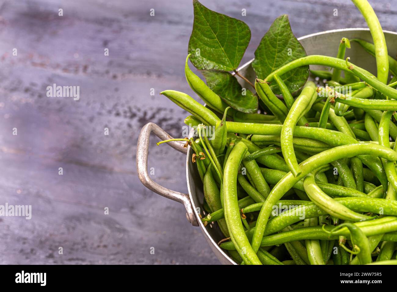 Grüne Bohnen in einem alten Sieb auf einem alten grauen Brett. Stockfoto