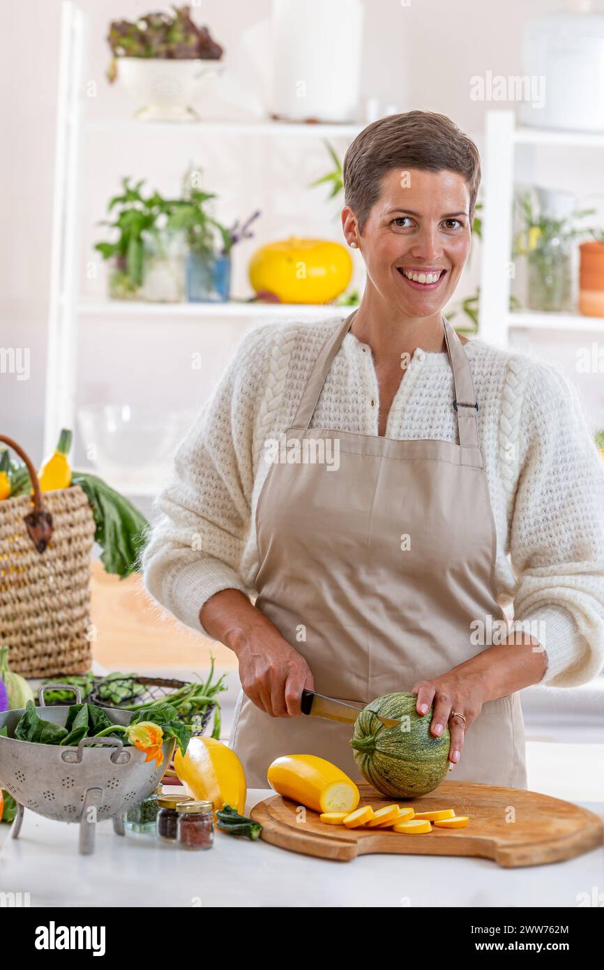 Junge Frau mit Küchenschürze umgeben von Bio-Gemüse. Stockfoto