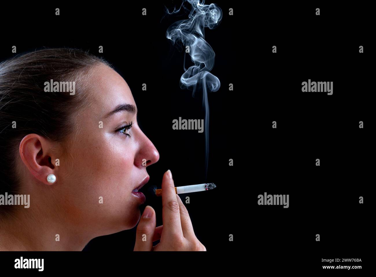 Nahaufnahme einer Frau, die eine Zigarette vor schwarzem Hintergrund raucht und raucht. Stockfoto
