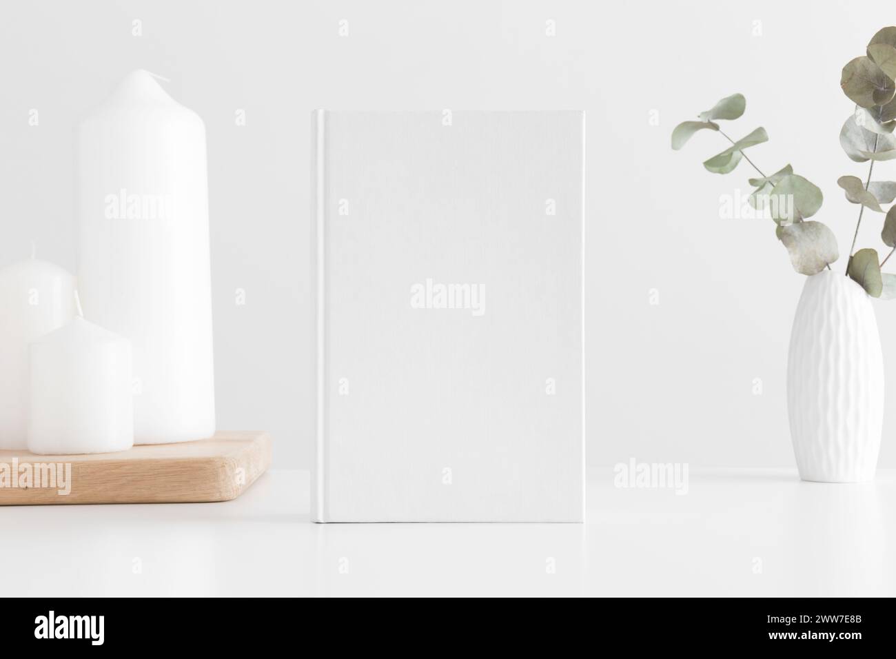 Weißes Buch-Mockup mit einem Eukalyptus in einem Topf und Kerzen auf einem weißen Tisch. Stockfoto