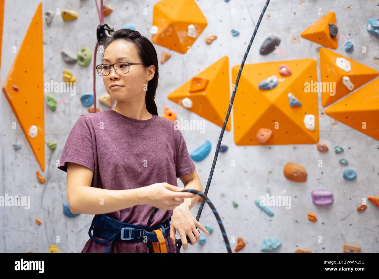 Eine junge Asiatin auf einer Kletterwand. Eine Koreanerin klettert auf eine Boulderwand. Attraktive Profi-Sportkletterer Frau, die im Fitnessstudio trainiert Stockfoto