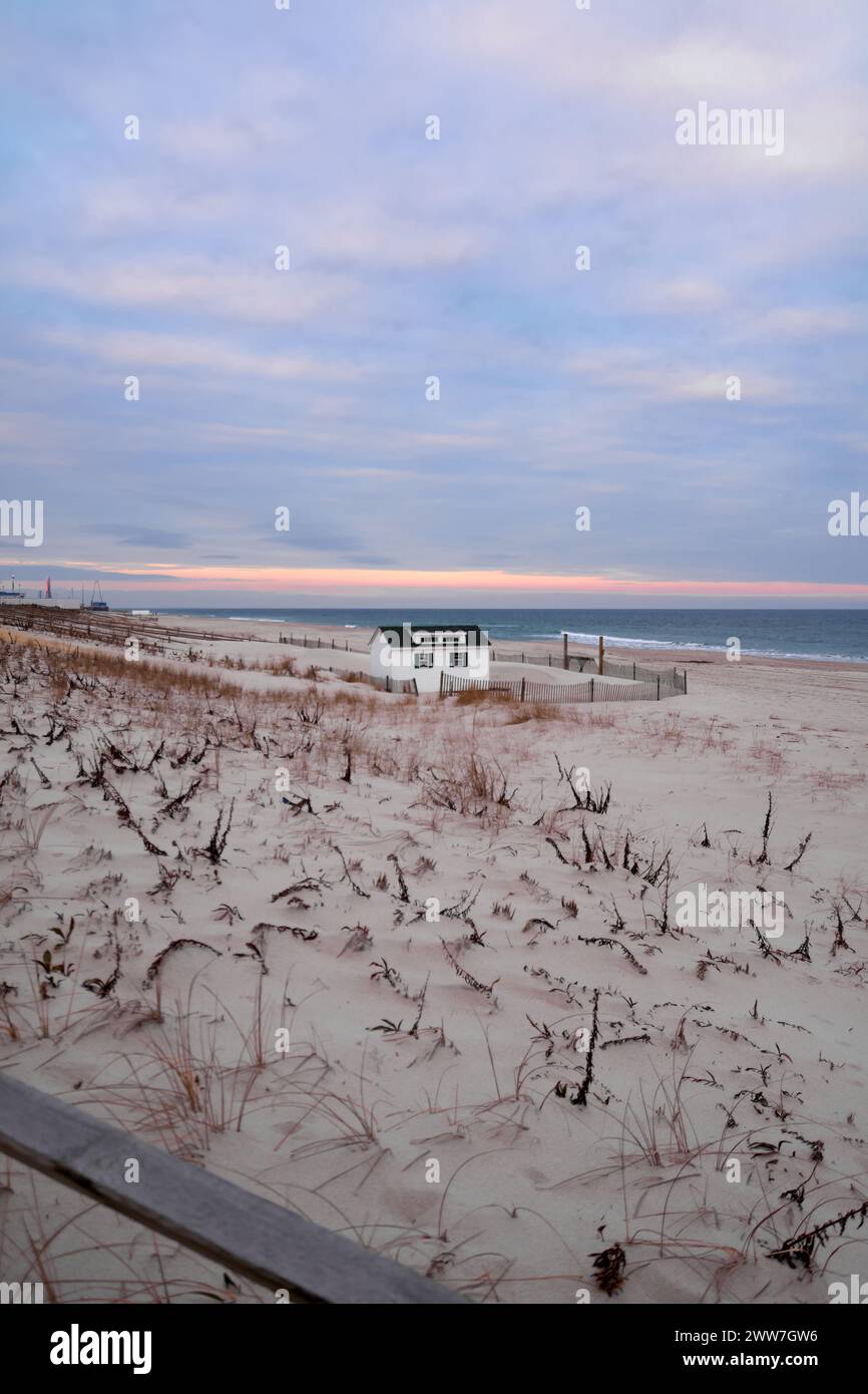 Eine einsame Hütte befindet sich an einem einsamen Strand, mit dem sanften Sonnenschein, der den Himmel erleuchtet und sich auf den ruhigen Wellen des Ozeans reflektiert. Stockfoto