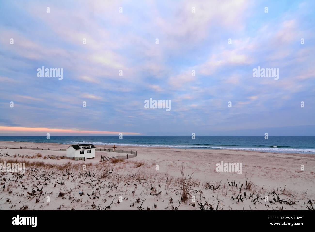 Die ruhige Szene eines Strandes bei Sonnenaufgang, mit einer kleinen Hütte, farbenfrohem Himmel und Küstenvegetation, die eine Atmosphäre der Ruhe und Gelassenheit schafft. Stockfoto