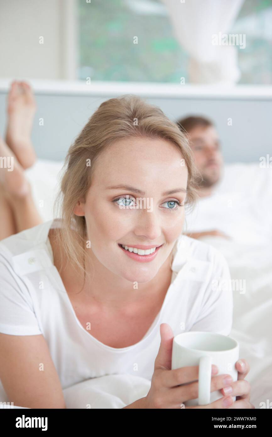 Frau auf Bett Holding Mug Stockfoto