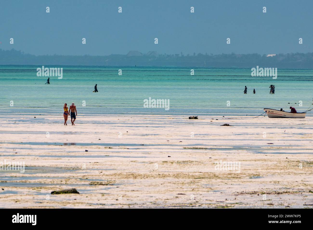Touristen spazieren am Strand bei Sonnenuntergang. Fotografiert an der Ostküste Sansibars Stockfoto
