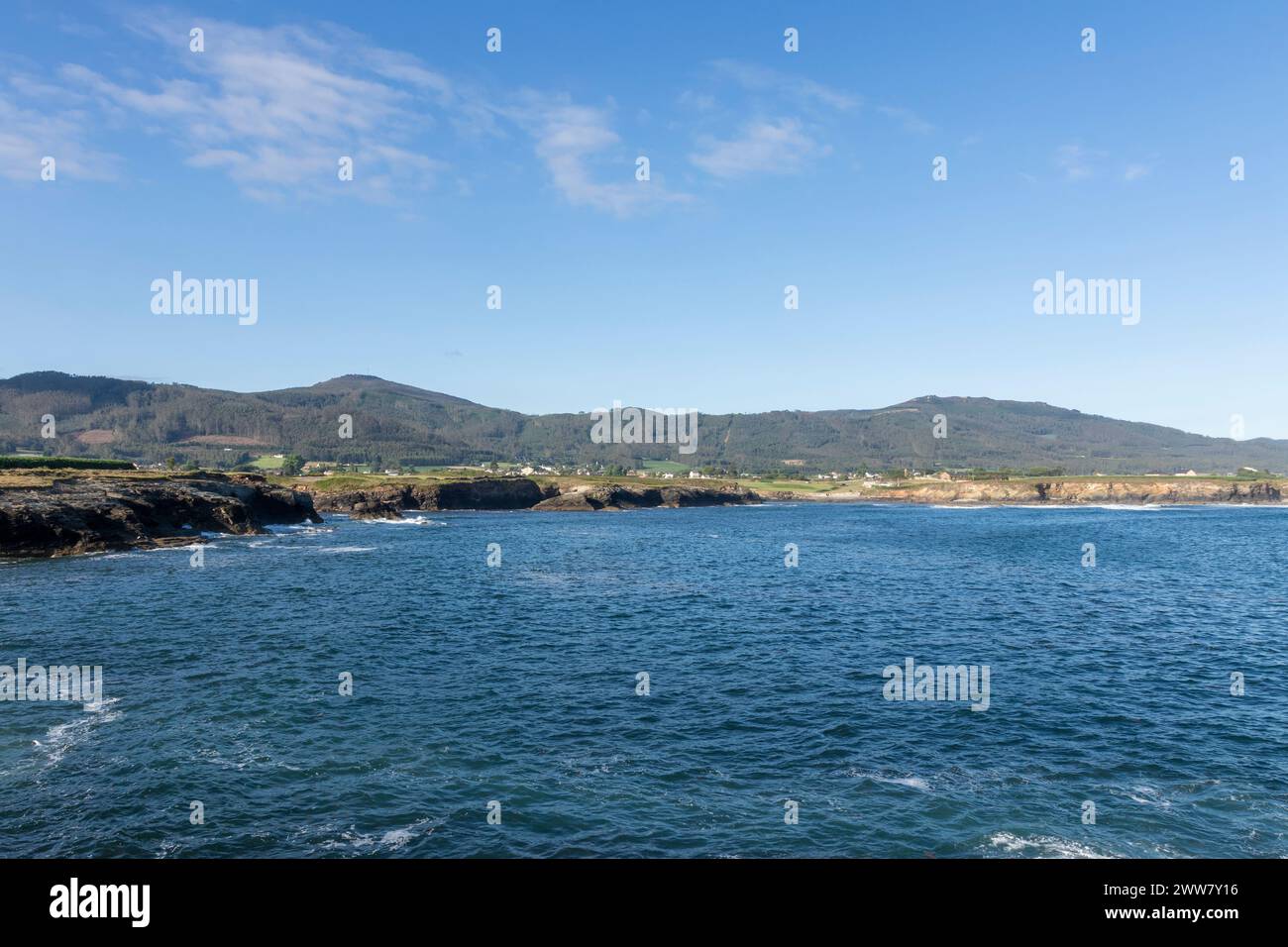 Ruhige Küstenlandschaft mit klarem Himmel, ruhigem Wasser und abgelegenen grünen Hügeln, die eine ruhige und malerische Aussicht bieten Stockfoto