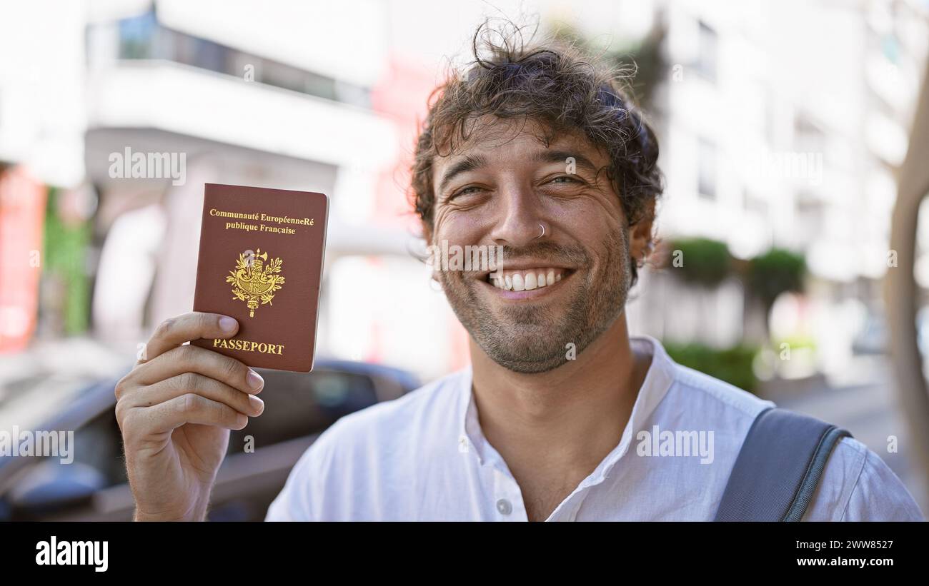 Hübscher bärtiger Mann mit grünen Augen, der einen französischen Pass auf einer sonnigen Straße hält. Stockfoto