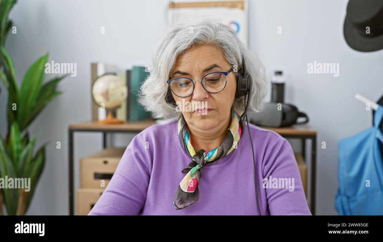 Porträt einer fokussierten, grauhaarigen Frau mit Kopfhörern in einem modernen Büro. Stockfoto