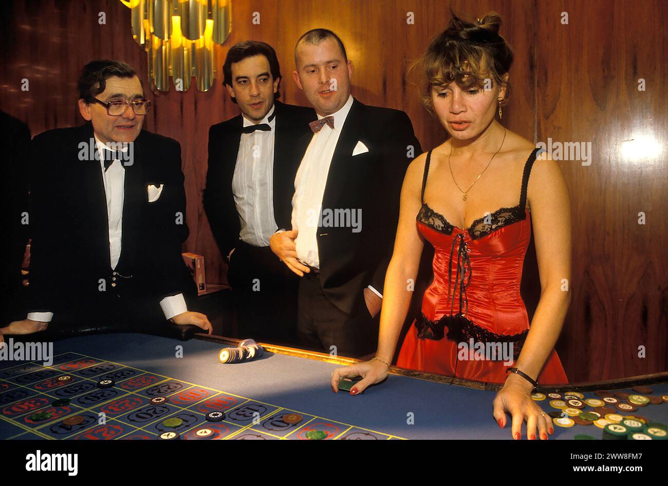 Roulette UK 1990s spielen Drei wären High Roller, wenn sie ihr Glück am Roulette-Tisch bei einem Spendenball im London Hilton on Park Lane hätten. Die Croupierin trägt ein burleskes Korsett baskisch. London, England ca. Dezember 1992. Stockfoto