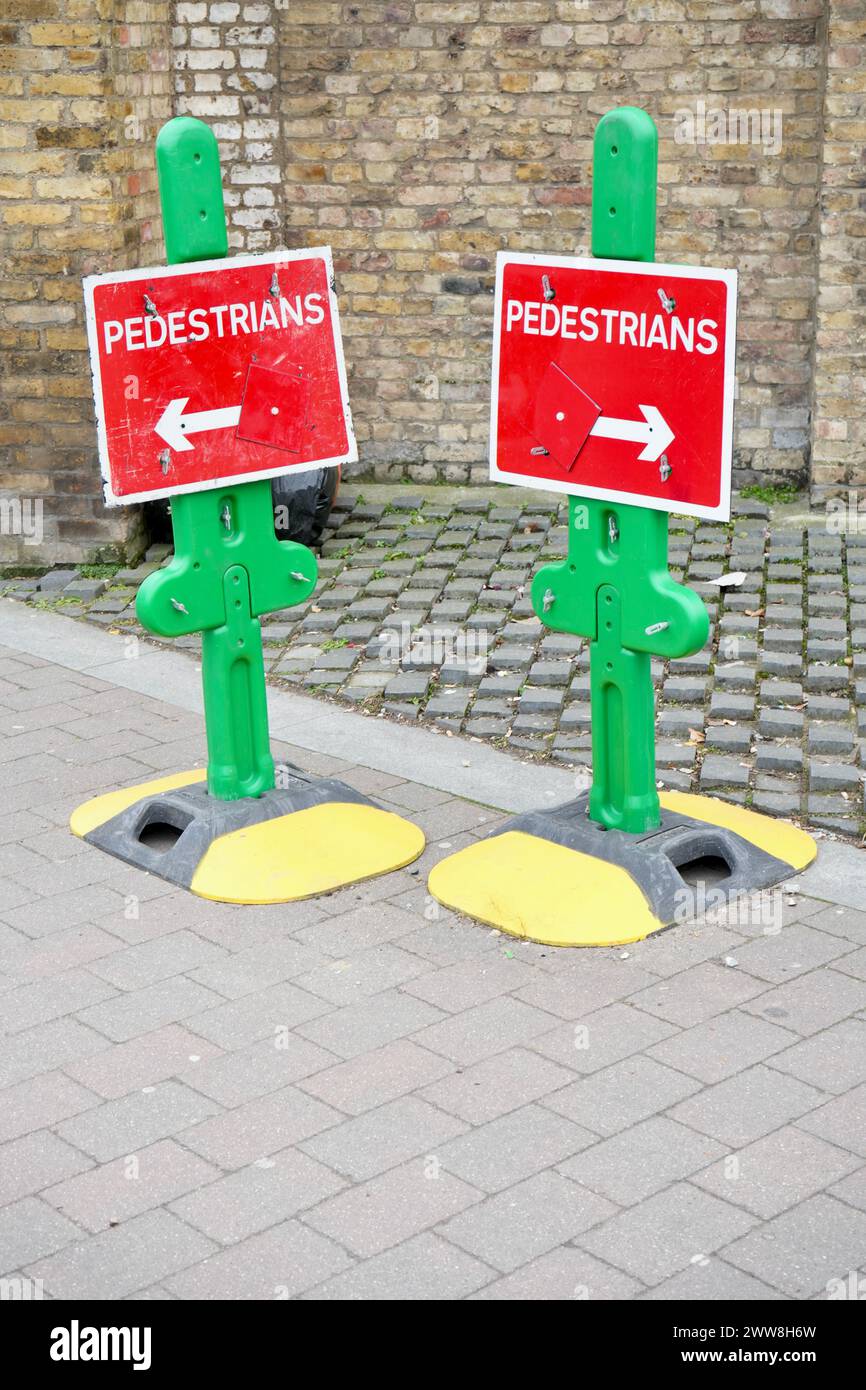 Farbenfrohe rote und grüne Fußgängerpfeilschilder auf gelben und schwarzen Ständen. Stockfoto