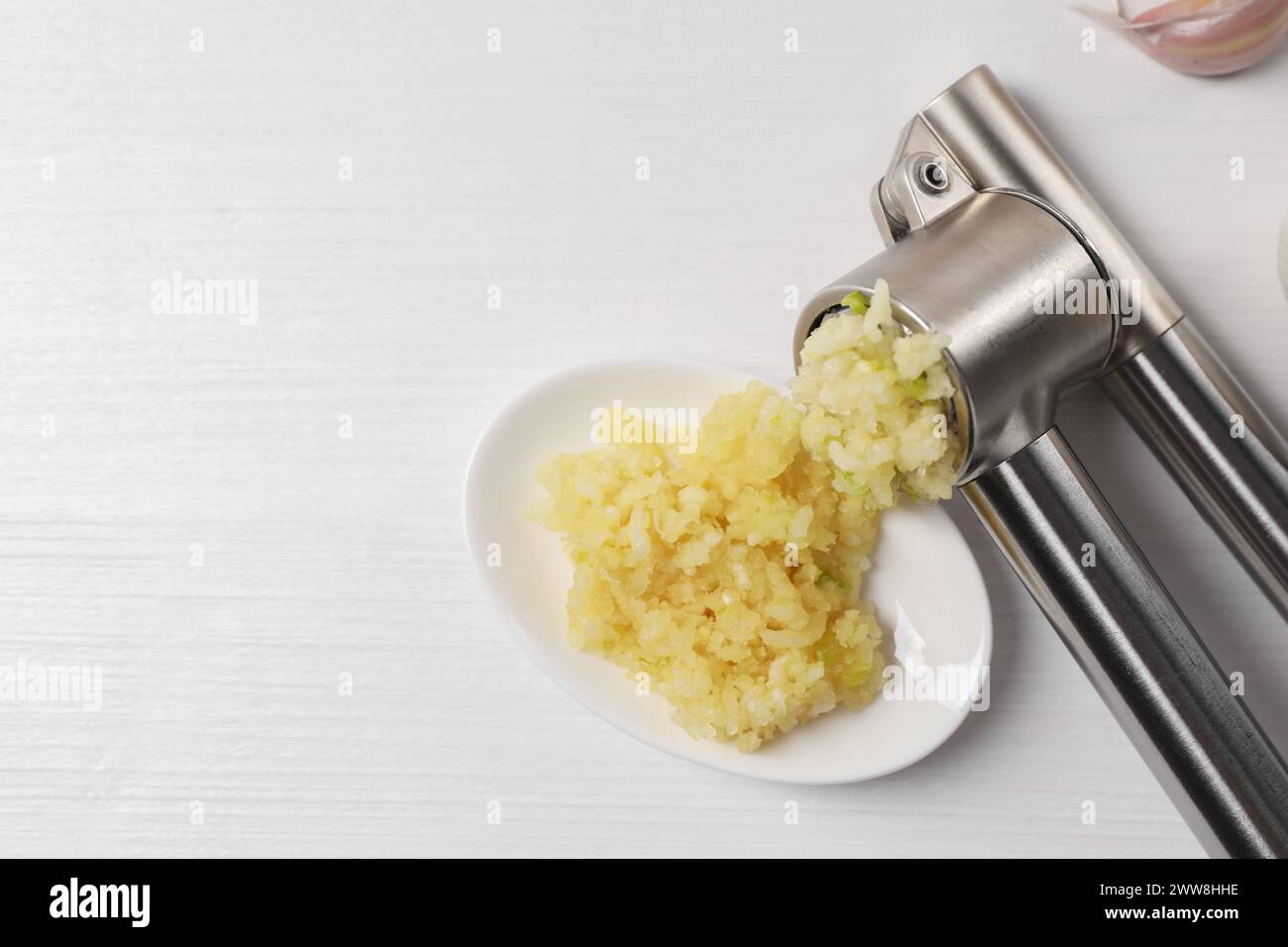 Eine Metallpresse und zerkleinerter Knoblauch auf weißem Holztisch, Blick von oben. Leerzeichen für Text Stockfoto