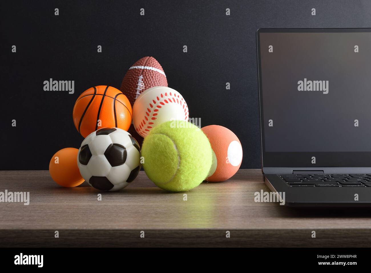 Konzept der Sportunterhaltung im Internet mit einem Laptop und Bälle verschiedener Sportarten auf einem Bürotisch. Vorderansicht. Stockfoto