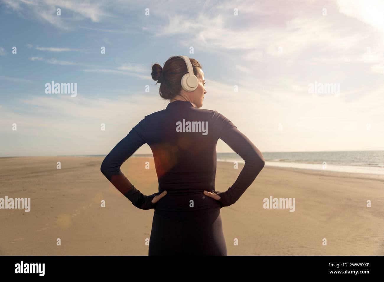 Rückansicht einer sportlichen Frau mit den Händen auf der Hüfte, die nach dem Training am Strand ruht Stockfoto