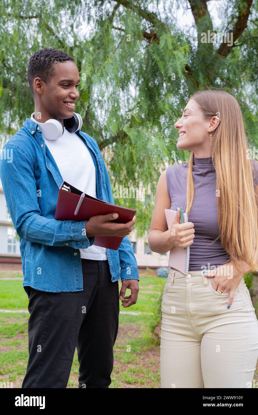 Vertikales Porträt lächelnde College-Freunde, die Notizen anschauen, reden und lachen auf dem Campus. Stockfoto