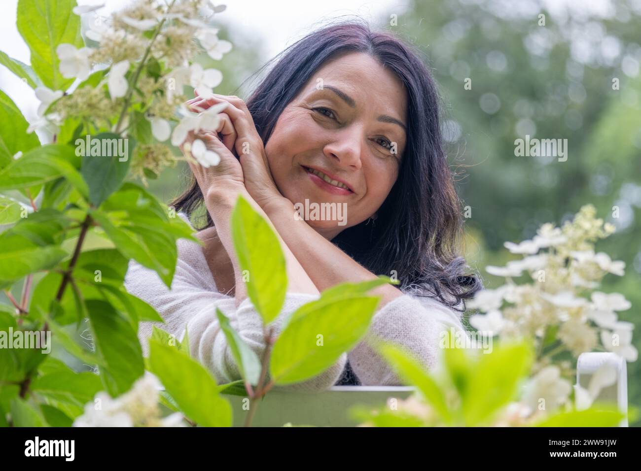 Eine lächelnde Midage-Frau in einem grünen Blumengarten drückt Glück und Freude über hormonelle Veränderungen und Kämpfe aus. Hochwertige Fotos Stockfoto