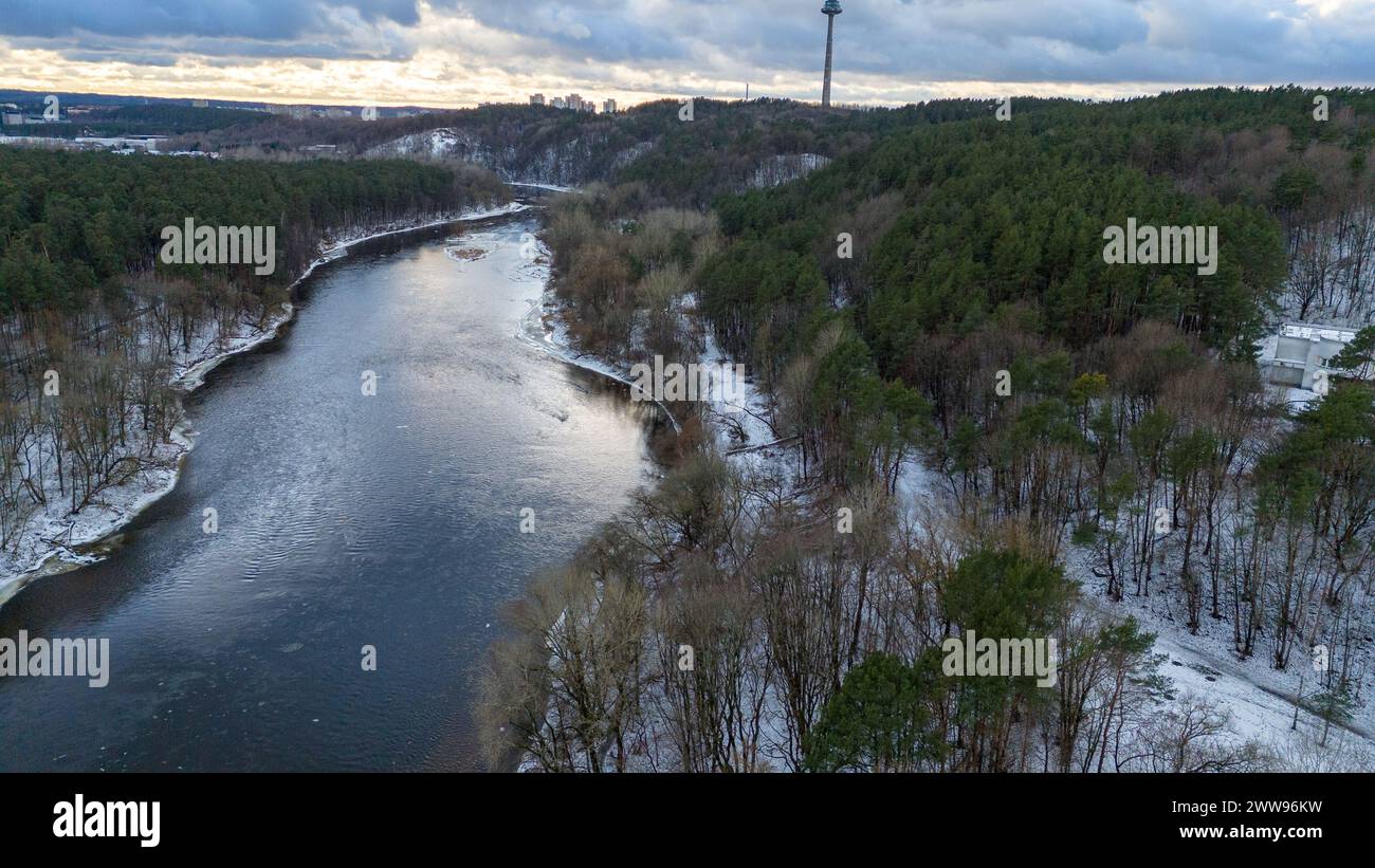 Drohnenfotografie des Flusses, der durch Park, Wald und Stadt fließt, am Horizont während des bewölkten Wintertages Stockfoto