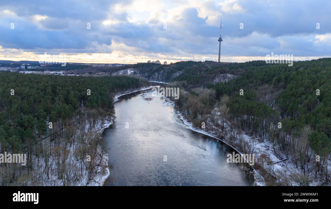 Drohnenfotografie des Flusses, der durch Park, Wald und Stadt fließt, am Horizont während des Winters Stockfoto