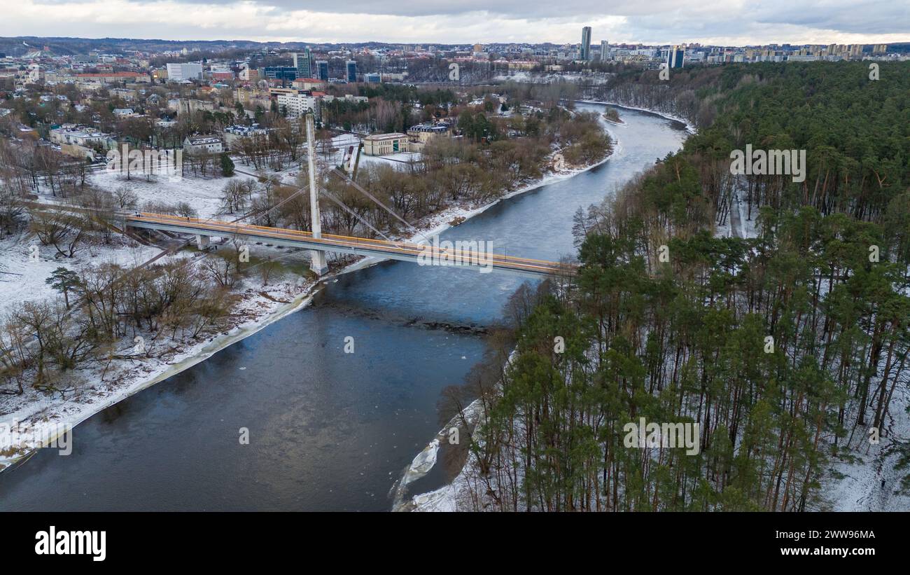 Drohnenfotografie einer Fußgängerbrücke über den Fluss von der Stadt in den öffentlichen Park während des bewölkten Wintertages Stockfoto