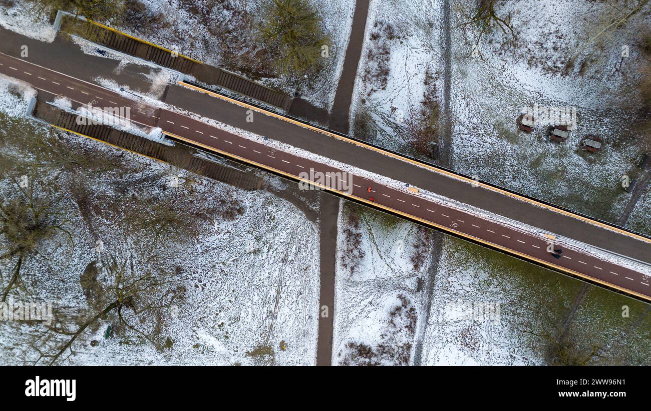 Drohnenfotografie einer Fußgängerbrücke über den Fluss von der Stadt in den öffentlichen Park während des bewölkten Wintertages Stockfoto