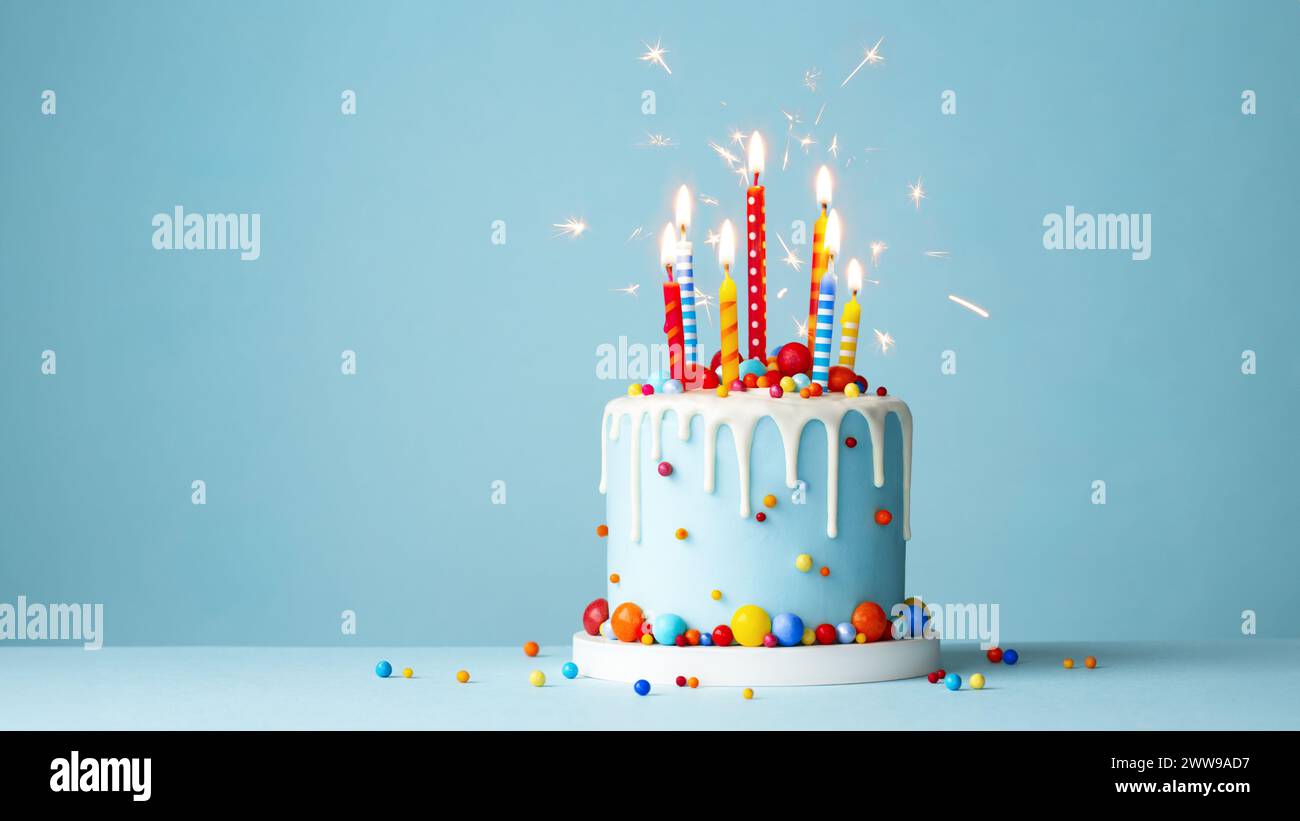 Bunte Geburtstagskuchen mit bunten Geburtstagskerzen und Glitzern vor blauem Hintergrund Stockfoto