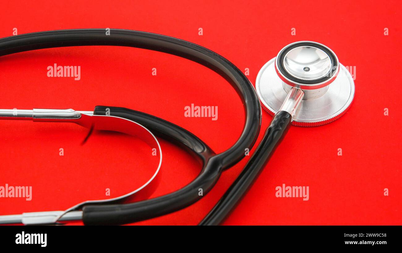 Ein Stethoskop, das auf den medizinischen Beruf hinweist, ist auf einem unberührten roten Hintergrund angeordnet Stockfoto