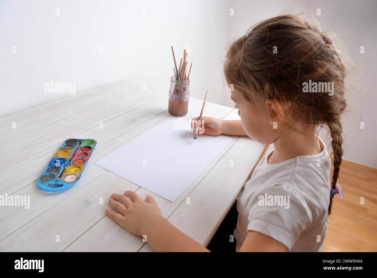 Das kleine Mädchen malt mit Wasserfarben auf weißem Papier. Vorstellung von Kreativität, Kunst, Kindheit, Fantasie und künstlerischem Ausdruck Stockfoto