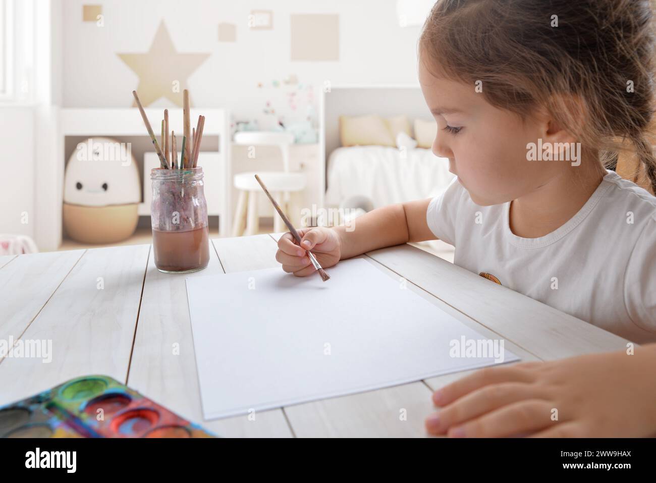 Ein junges Mädchen malte mit Aquarellen auf weißem Papier in ihrem Zimmer. Ideal für die Kreativität von Kindern oder künstlerische Konzepte Stockfoto