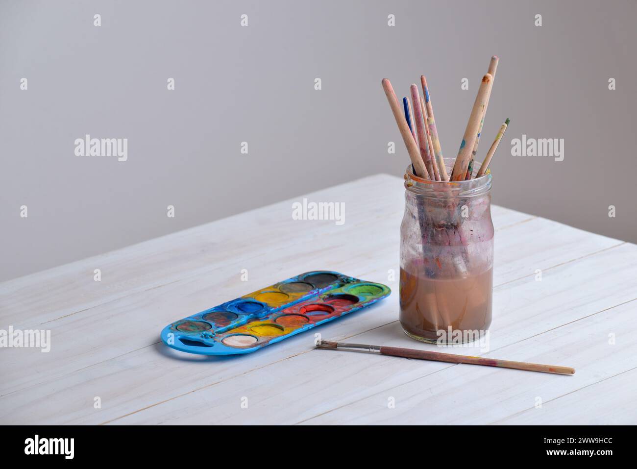 Becher mit Pinseln auf Arbeitstisch mit Aquarellen. Leerzeichen beiseite kopieren. Ideal für Kunstbedarf, Kreativität oder Malkonzepte Stockfoto