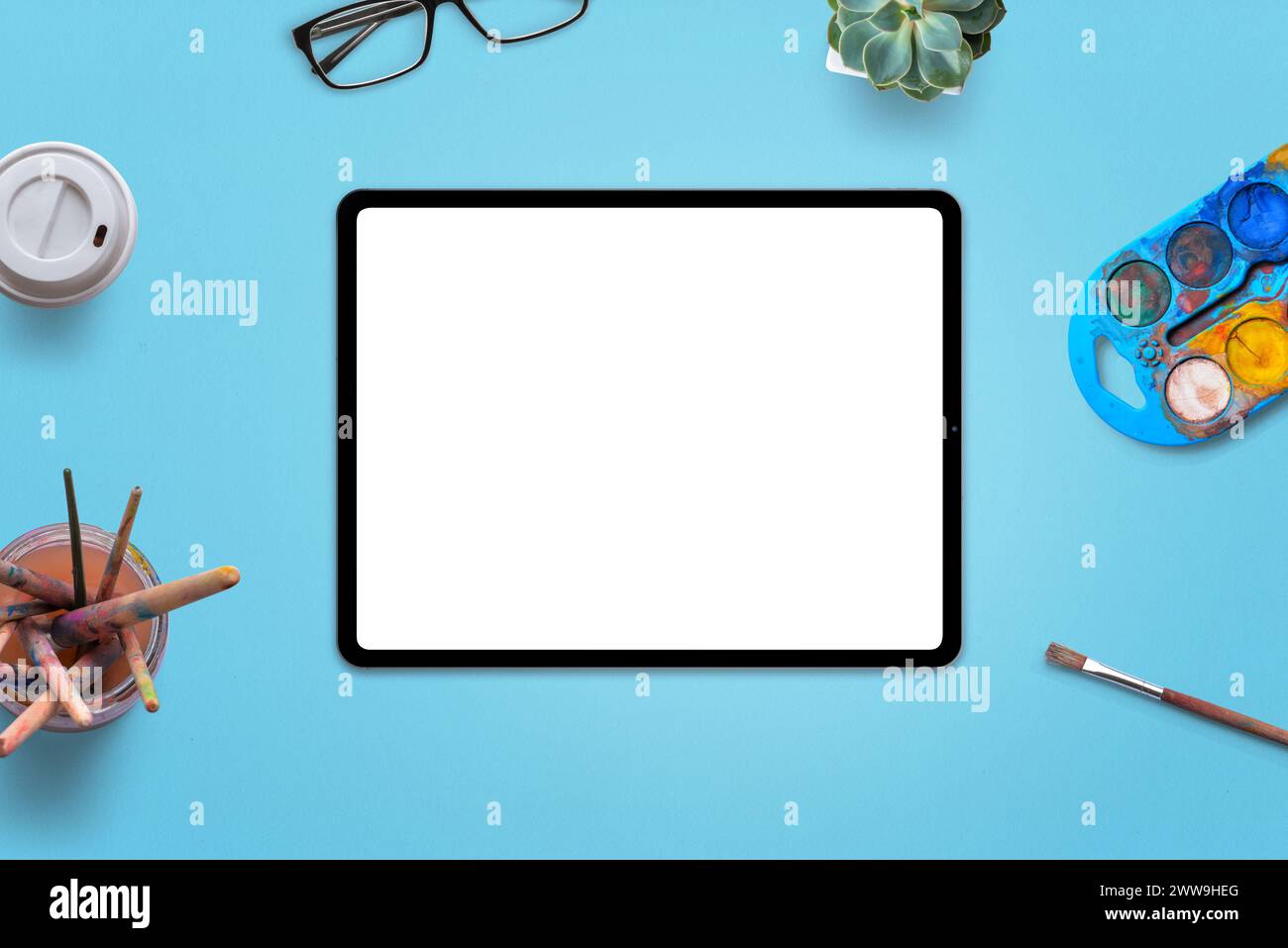 Isoliertes Tablet auf dem Schreibtisch mit weißem Bildschirm, umgeben von Pinseln und Aquarellen. Kunstbegriff und Arbeit auf einem Tablet Stockfoto