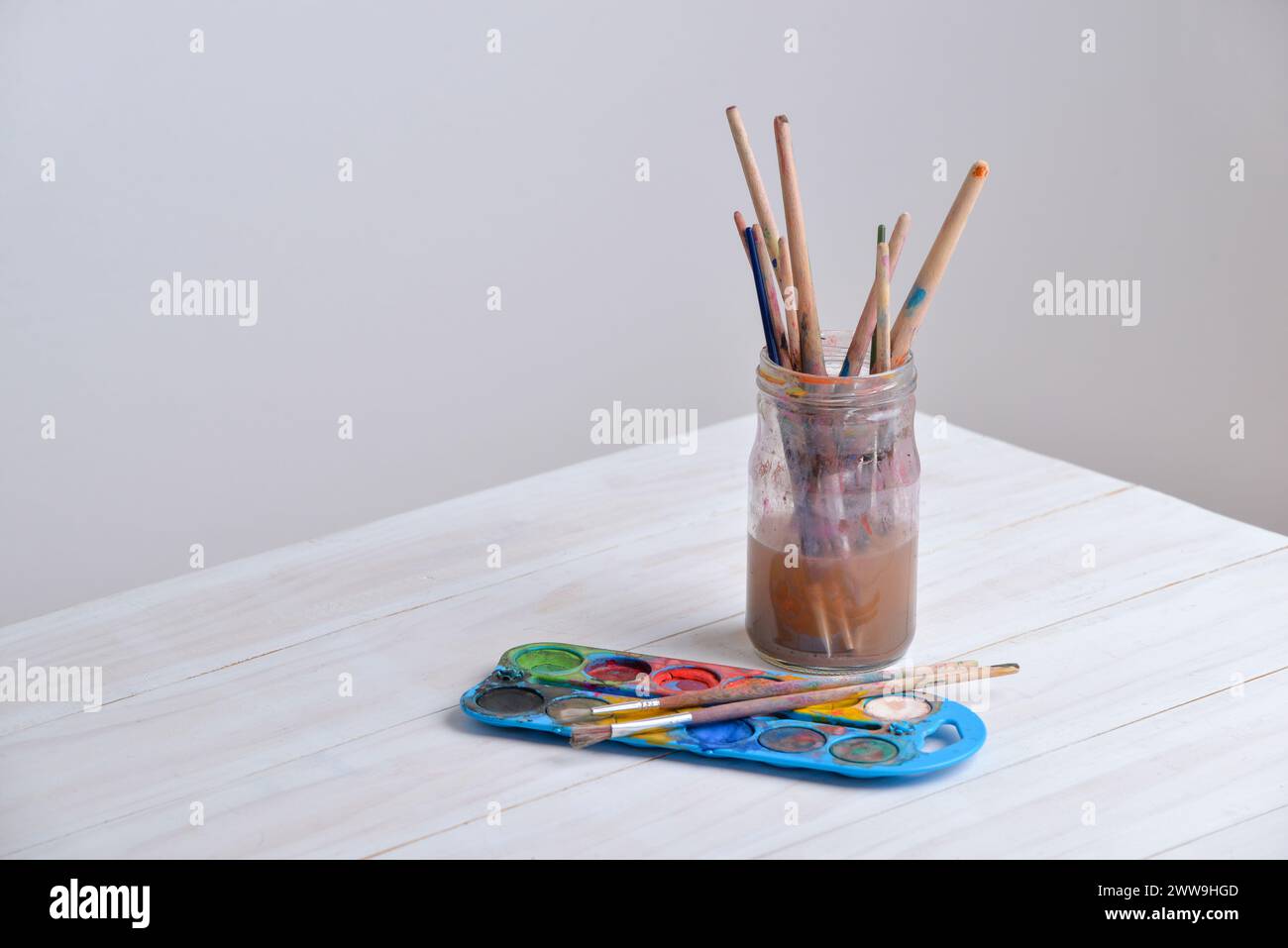 Glas mit Pinseln und Aquarellen auf Holztisch. Ideal für kreative Projekte oder künstlerische Themen Stockfoto