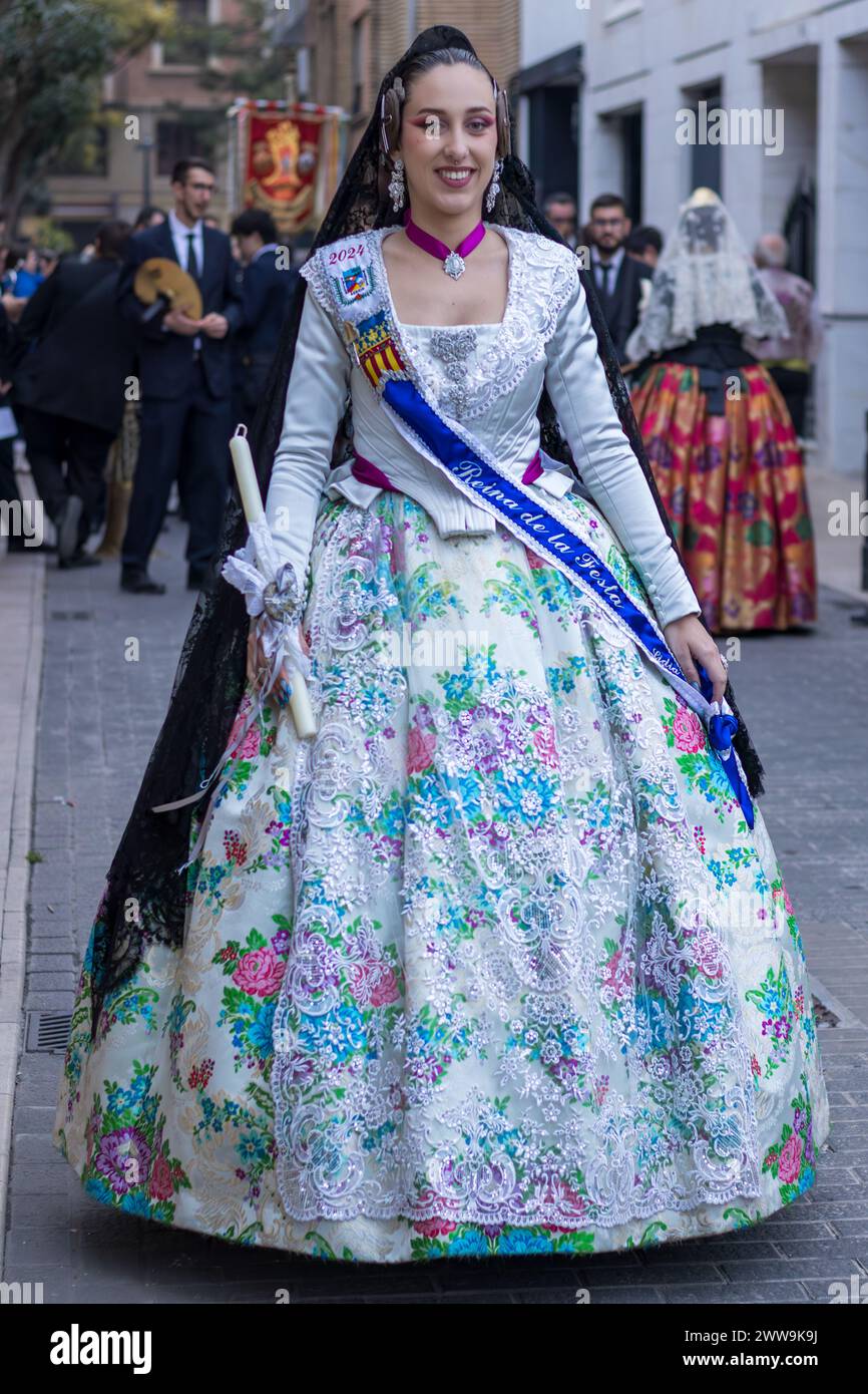Eine Frau in traditionellem valencianischen Kleid besticht mit ihrem Kleid mit Blumenmuster während der lebhaften Feierlichkeiten in Gandia. Ihre Kleidung, eine Leinwand voller Hi Stockfoto
