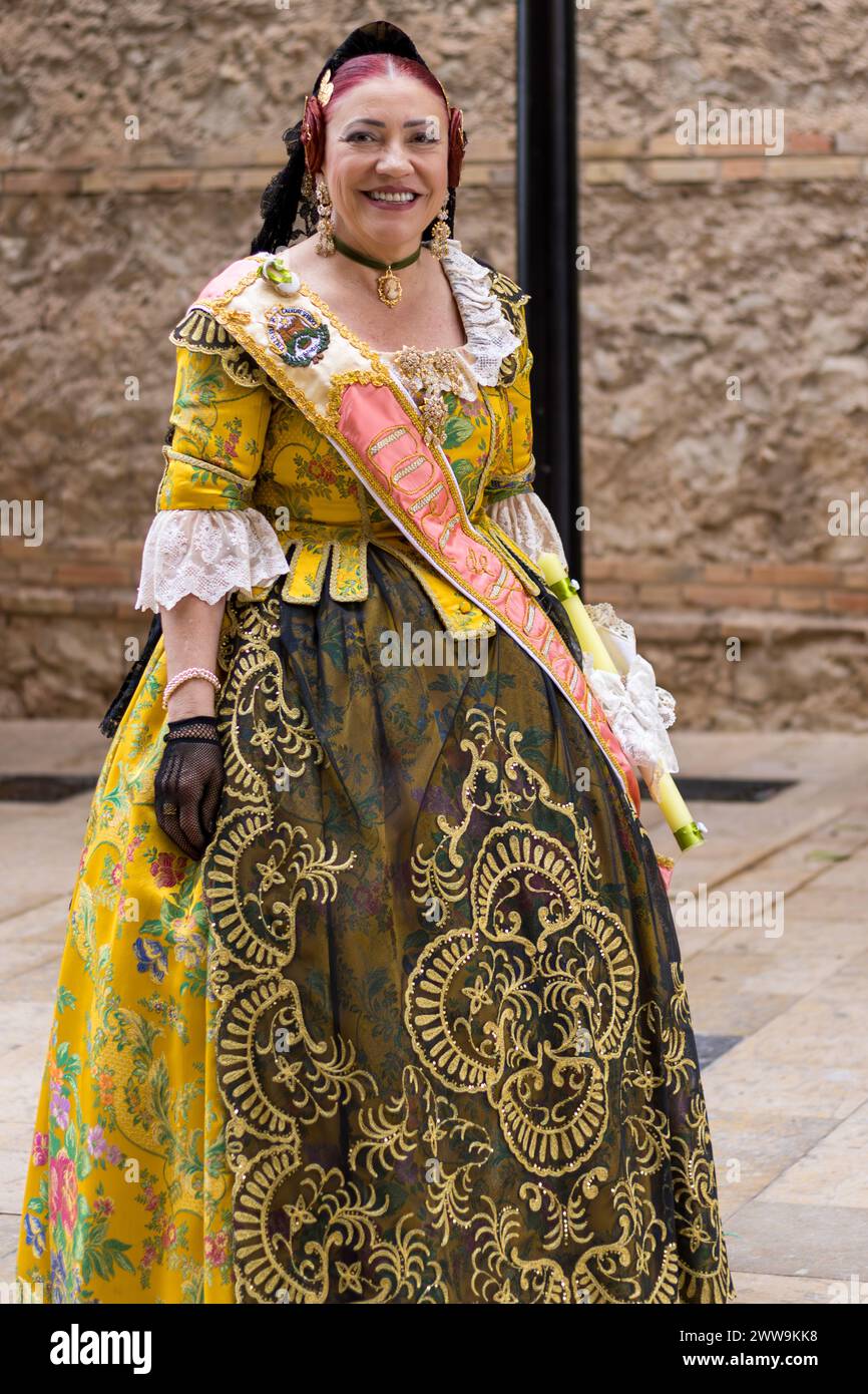 Valencianische Pracht in Gandias Fallas blüht die Kleidung einer Frau voller kultureller Geschichten. Ihr leuchtendes gelbes Kleid mit traditionellen Mustern Stockfoto