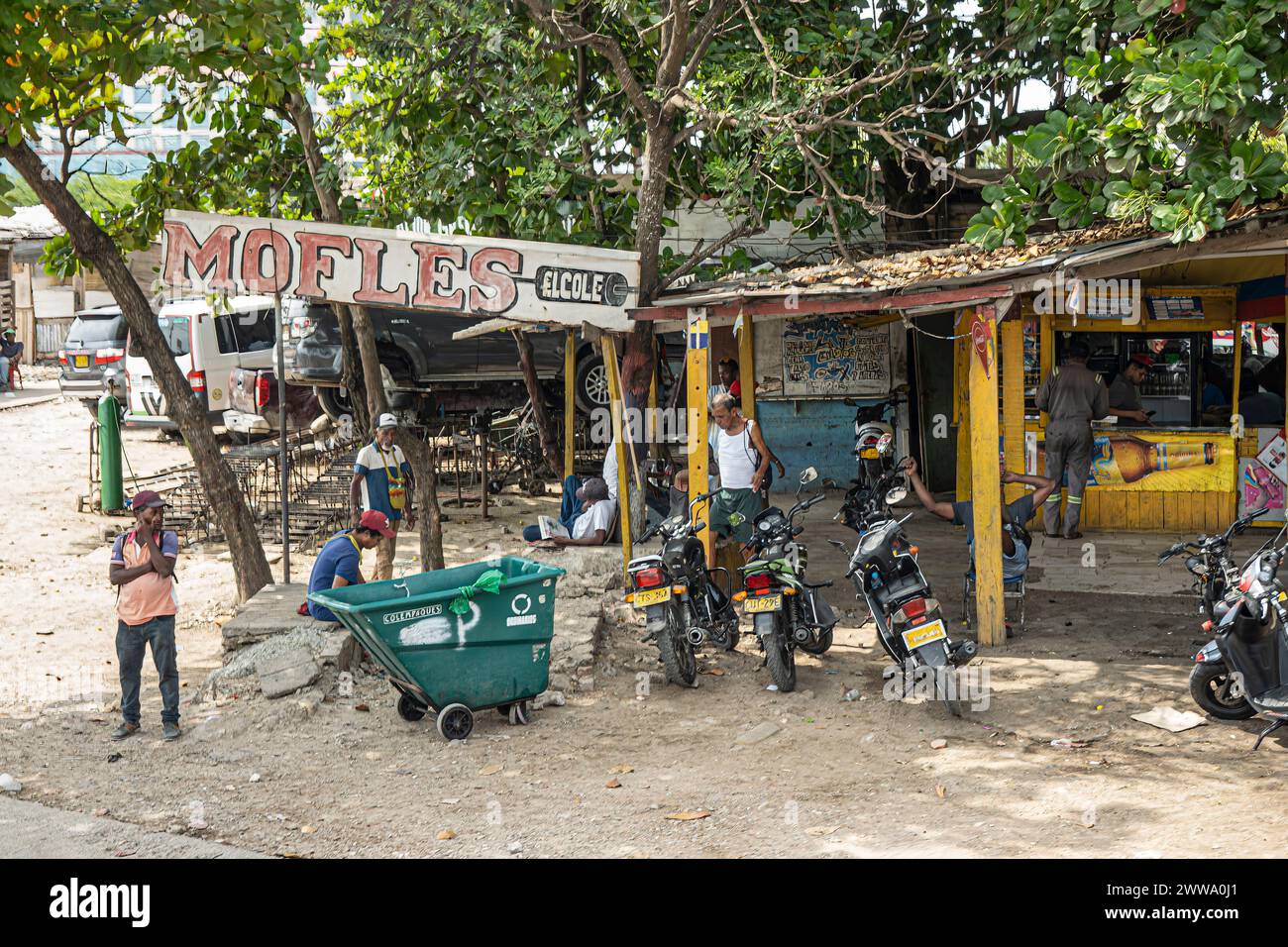 Cartagena, Kolumbien - 25. Juli 2023: Straßenecke installieren und repais Motorradschalldämpfer, wo andere Anbieter Bier und Snacks in einer Hütte verkaufen Stockfoto