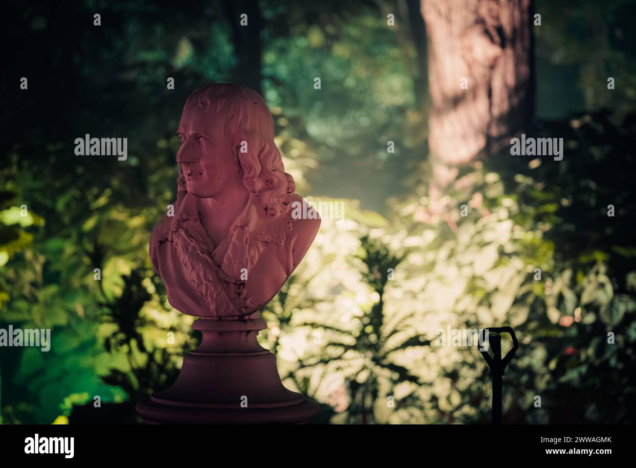 Eine leise beleuchtete Büste von Voltaire in einem Garten, die historische und philosophische Betrachtungen ausstrahlt. Stockfoto