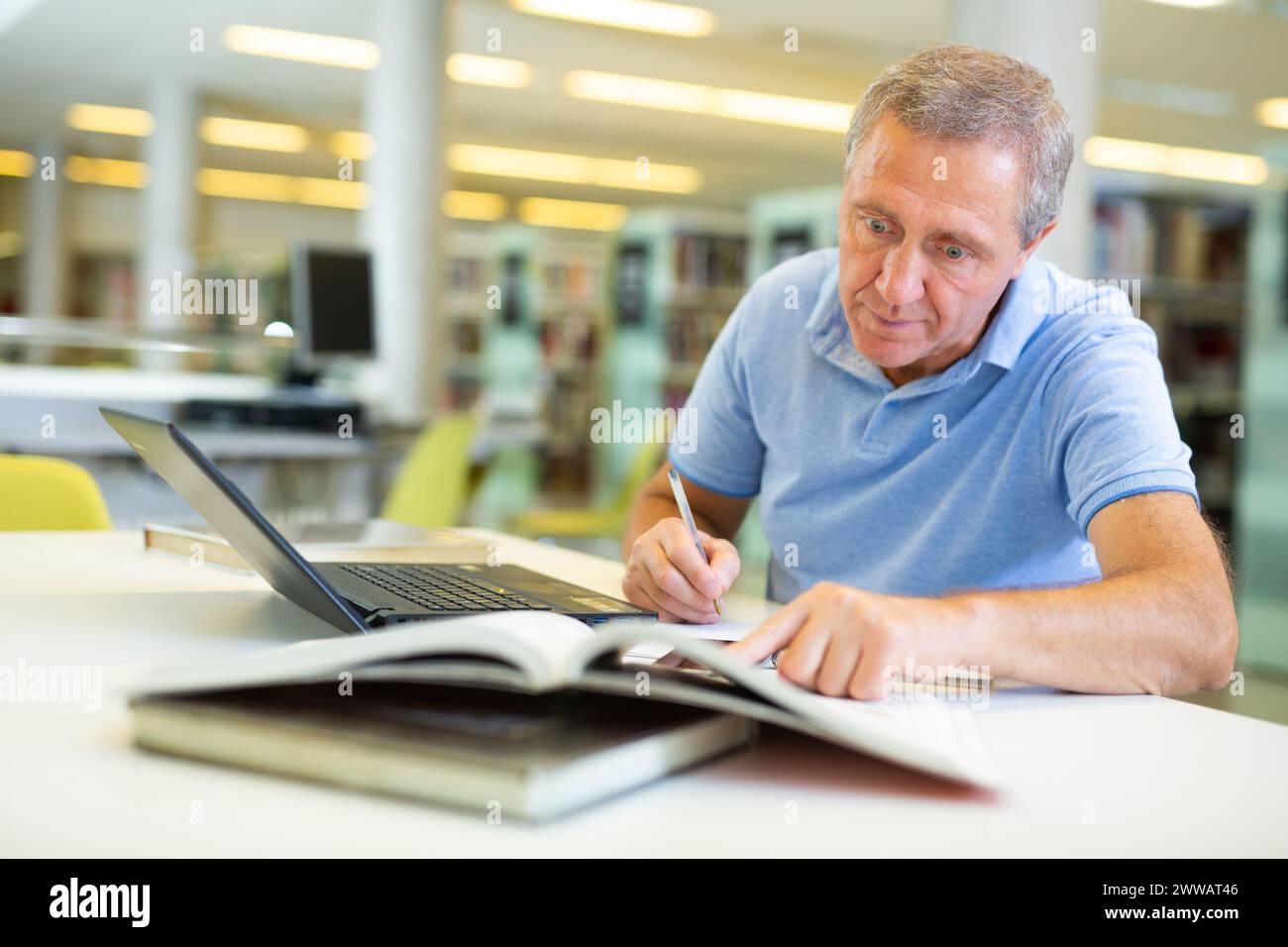 Porträt eines älteren Mannes mit Laptop und Buch in der Bibliothek Stockfoto